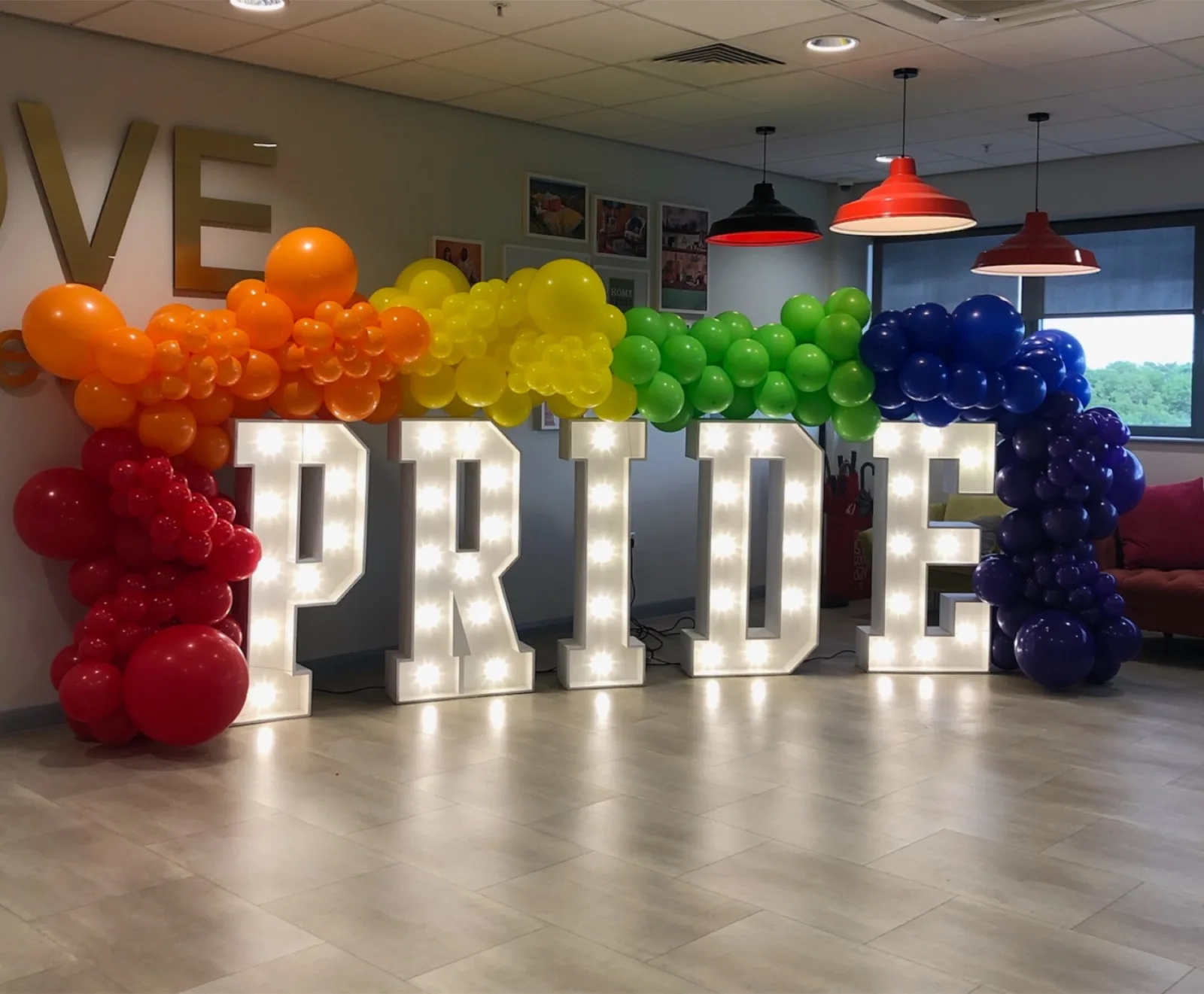 White light up letters spelling PRIDE with rainbow balloons